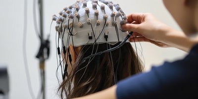 [Translate to English:] Forschende setzen einer Probandin eine EEG-Haube mit zahlreichen Elektroden auf, um Gehirnaktivität zu messen