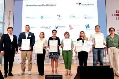 Stefan Remy is standing on stage with other representatives of the Leibniz Association and presenting the certificate for the ‘Work and Family’ audit.