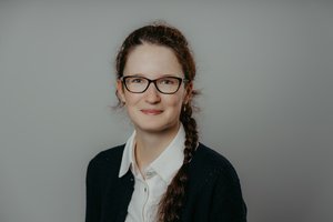 Portrait of a young woman against a dark background, photographed head-on and smiling warmly.