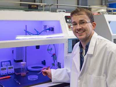Michael Schleyer mit Kittel im Labor setzt Fruchtfliegen in eine Petrischale