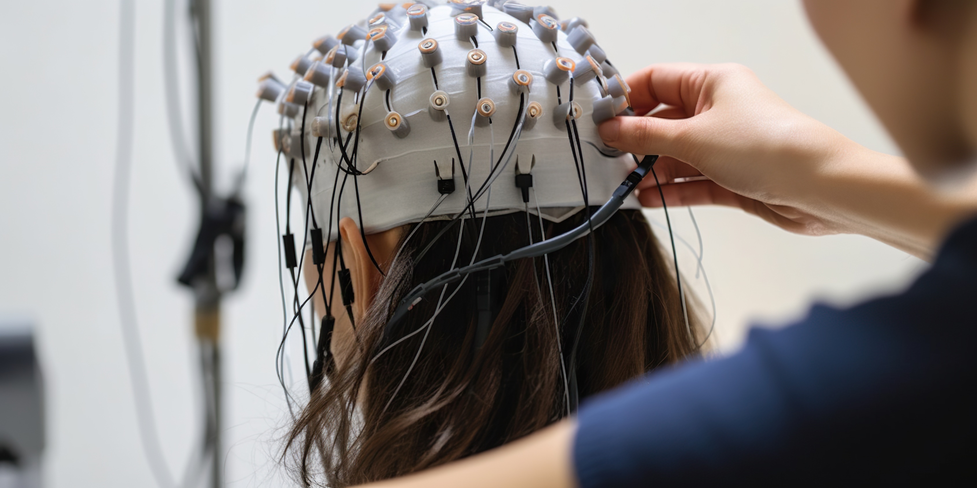 [Translate to English:] Forschende setzen einer Probandin eine EEG-Haube mit zahlreichen Elektroden auf, um Gehirnaktivität zu messen